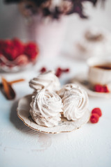Still life of the homemade Marshmallow zephyr on plate with raw raspberries and a cup of tee on a white table.