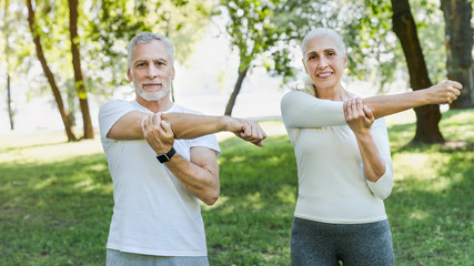 Senior couple stretching in park outdoors before yoga and fitness exercises