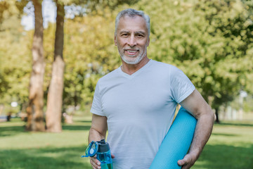 Active senior man with bottle water and carpet after workout in park, health care, sport