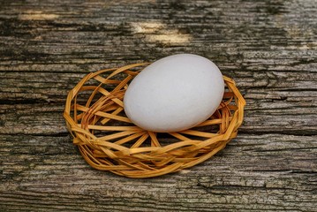 one white egg lies in a brown decorative basket on a gray table
