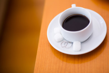 wedding rings on a saucer with a cup of coffee and pieces of sugar