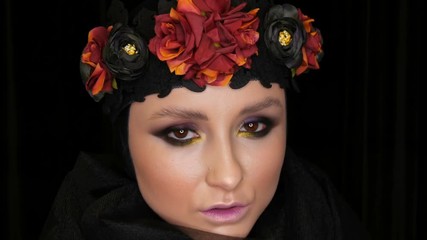 Professional girl model with beautiful makeup poses in a black cap and wreath on her head in front of the camera on a black background in the image of a black widow. High-fashion