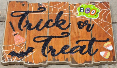 Trick or treat text on a plaque with boo message, bat, candy, witches broom close up on wood background, nobody, 