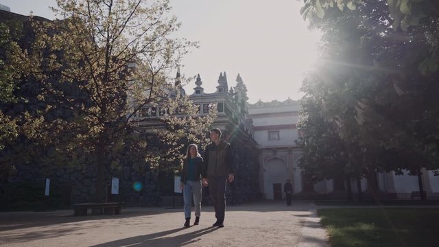 loving couple walk holding hands in palace park in rays of evening sun