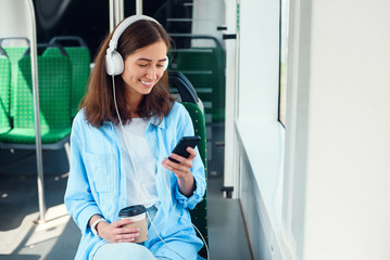 Young woman using public transport sits with smart phone and white headphones in the modern bus.