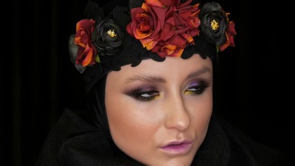 Professional girl model with beautiful makeup poses in a black cap and wreath on her head in front of the camera on a black background in the image of a black widow. High-fashion