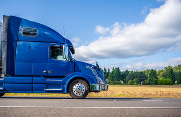 Big rig blue semi truck transporting cargo in semi trailer driving on the flat road with yellow...