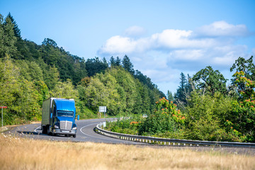 Big rig bonner blue semi truck with semi trailer transporting cargo running on the winding road...