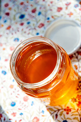 Open jar with fresh yellow organic bio honey on the colorful floral table