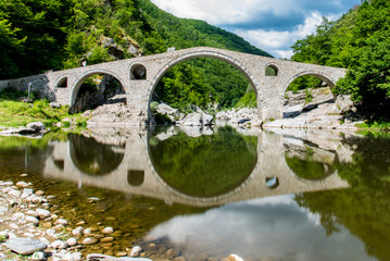 Fototapeta na wymiar Ancient bridge in the mounbtains with reflection in the water. Devil's bridge - Bulgaria