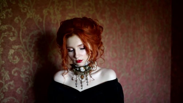 Dark halloween attire. Gothic woman is vampire with pale skin and red hair in a black dress and a necklace on her neck. Girl witch with red lips. Gothic look. Outfit for halloween. Clean skin