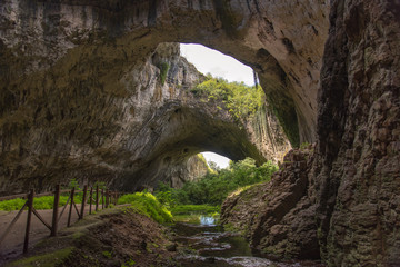 Odd beautiful cave with green plants inside and wholes in the ceiling with blue skies