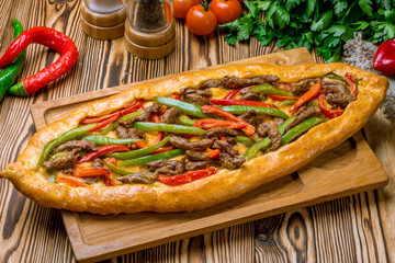 Turkish pide with vegetables and pieces of beef on wooden table