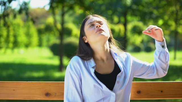 Young woman resting on bench in park, suffering from heat and stuffiness, pms