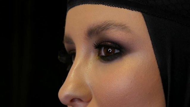 Professional girl model with beautiful makeup poses in a black cap on her head in front of the camera on a black background in the image of a black widow. High-fashion