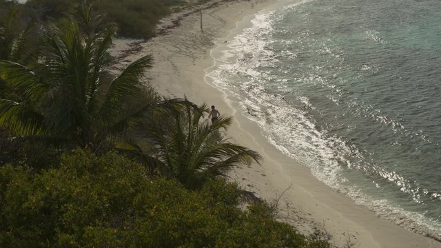Aerial view revealing distant couple running on ocean beach / Petit Tabac, Tobago Cays, St. Vincent and the Grenadines