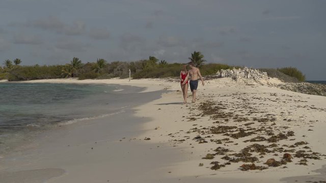 Panning shot of romantic couple walking on ocean beach / Petit Tabac, Tobago Cays, St. Vincent and the Grenadines