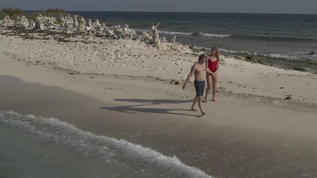 Aerial view of happy couple holding hands and walking on narrow beach / Petit Tabac, Tobago Cays, St. Vincent and the Grenadines