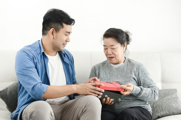 Happy Asian man giving gift box to his mother for Mother's Day celebration.