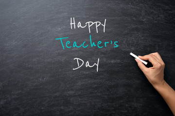 Education or back to school Concept. Woman hand holding chalk with Happy Teacher's Day text over chalkboard background.