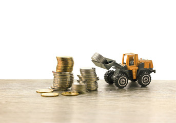Wheel loaders  heavy duty vehicle model construct the coins tower on wood table background , business and money construction concept..