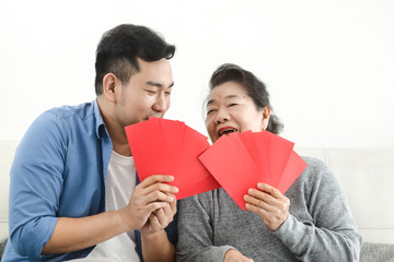 Happy Asian mother give red envelopes containing cash to her son for Chinese New Year concept.