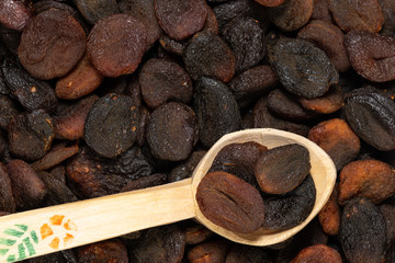 Closeup of dark brown colored dried apricots in a wooden scoop with selective focus