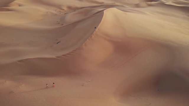 Aerial view from drone flying away from a walking young man to the top of a dune in Abu Dhabi desert, United Arab Emirates