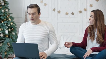 Aggressive young woman hindering man working on computer on remote workplace.