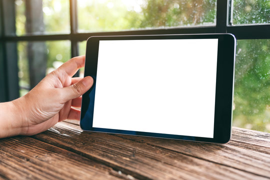 Mockup image of a hand holding black tablet pc with blank white desktop screen on wooden table