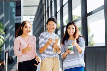 Smart smiling Asian women with notebooks and coffee gesturing thumb up and looking at camera in corridor