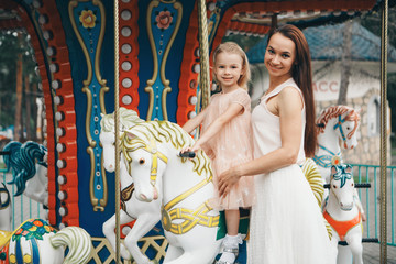 Fototapeta na wymiar a little girl with her mother riding in the Park on a toy horse on the carousel. Entertainment industry concept, family day, children's parks, playgrounds
