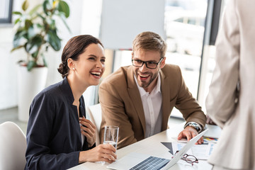 partial view of smiling businesspeople in formal wear at table during conference in office