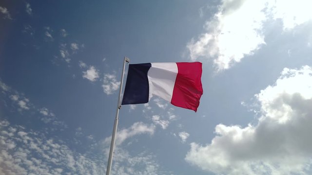 Slomo footage of French flag waving from a flagpole on a sunny day, seen from below.