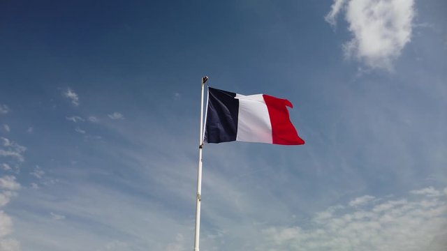 Slow motion footage of French flag swaying in the wind with blue sky in the background.