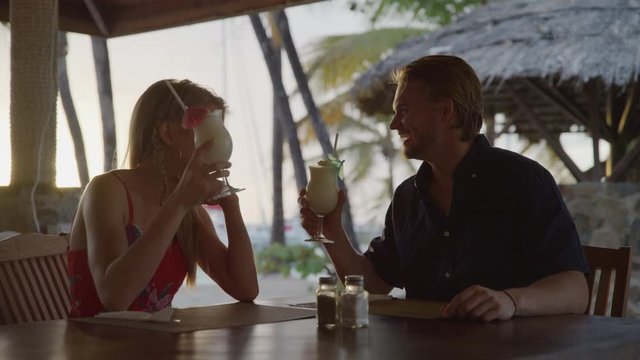 Romantic couple toasting with cocktails at beach restaurant / Salt Whistle Bay, Mayreau, St. Vincent and the Grenadines