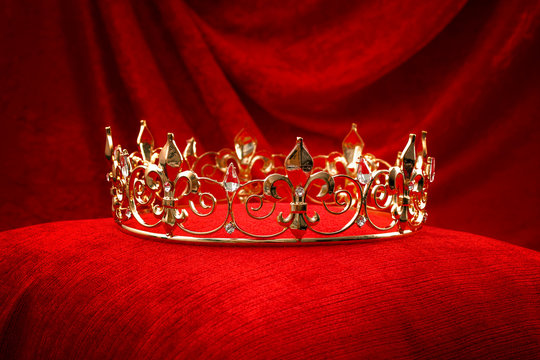 Royalty, monarch coronation or leadership conceptual idea with king gold crown with jewels on red velvet pillow