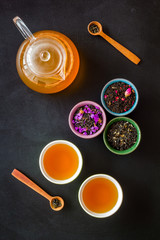 Cups, teapot, dry tea on black background top view