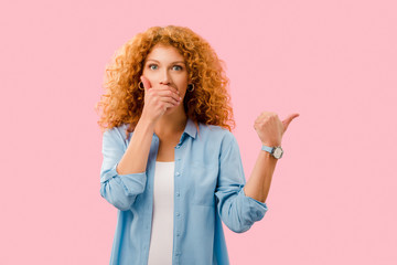attractive shocked redhead girl pointing isolated on pink