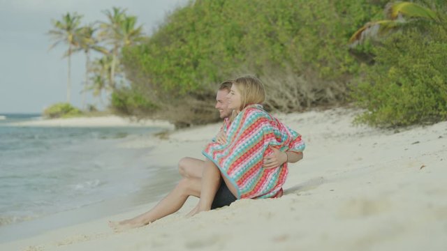 Romantic couple sitting on beach wrapped in a blanket / Petit Tabac, Tobago Cays, St. Vincent and the Grenadines