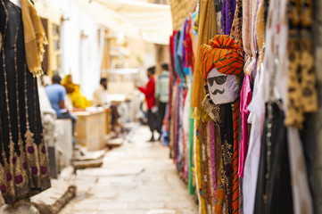 (Selective focus) Beautiful shop with colorful traditional Indian clothes (Sari) and a mask depicting a person's face from Rajasthan. Jaisalmer, India.