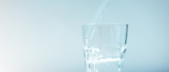 Close-up of stream of water filling glass on a pale blue background