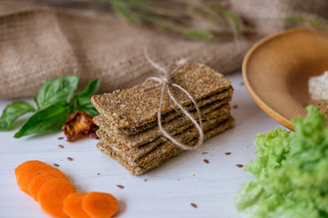 Crispbread tightened by a rope. Healthy food on a white background besid the ingredients in a wooden plate. .Lettuce with carrot near bread cakes