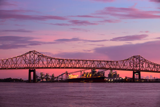 Steel bridge over Mississippi river under a stunning sunset sky in Baton-Rouge, Louisiana, with freight vessel and plant in the background