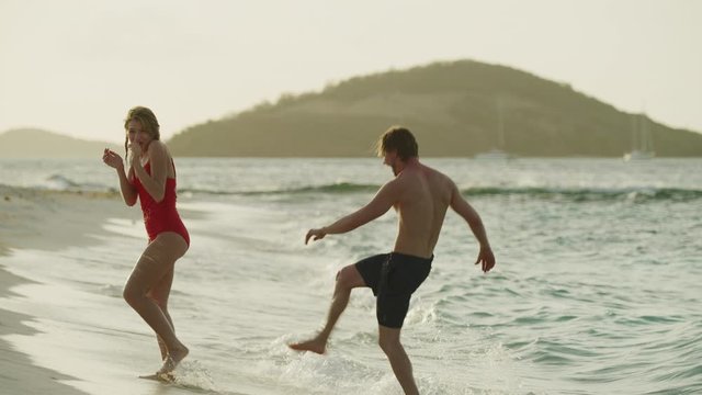 Playful couple splashing each other on ocean beach / Petit Tabac, Tobago Cays, St. Vincent and the Grenadines
