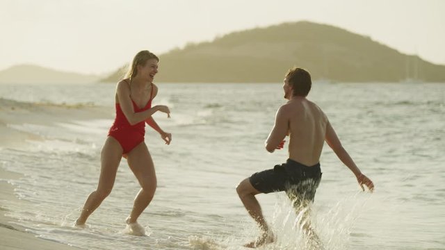 Playful couple splashing each other on ocean beach / Petit Tabac, Tobago Cays, St. Vincent and the Grenadines