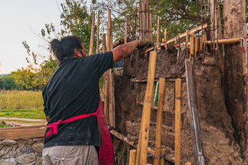 close up photography of a man and a woman working on a wall made of mud and glass bottles, outdoors on a sunny day