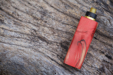 high end red natural stabilized wood regulated box mods with rebuildable dripping atomizer on natural timber wood texture background, vaporizer equipment, selective focus