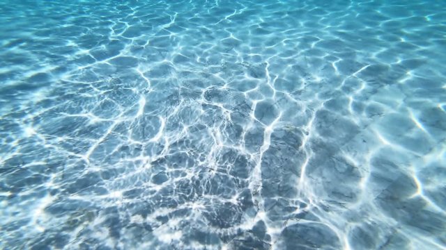 Sunlight makes patterns on the bottom of a pool as it passes through the clear blue water. Bright tropical sunshine and warm water make a relaxing scene.