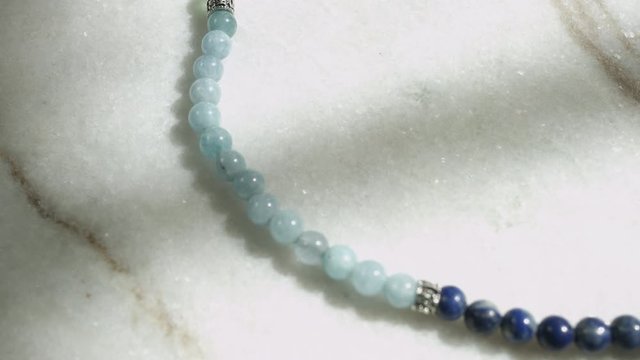Dolly macro shot of blue Celestite beads from Tibetan prayer mala placed on white marble shot in UHD